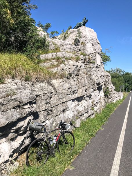 A bicycle parked by a rocky outcrop alongside a cycling path on a sunny day.