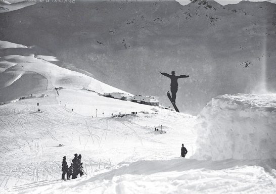 A skier mid-air jumping off a snow ramp with mountains in the background.