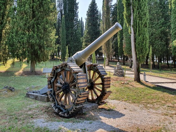 Old cannon on wheels, set in a grassy area surrounded by trees.