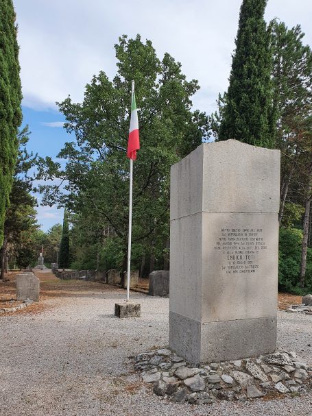 Monument in a park with a flagpole and surrounding trees.