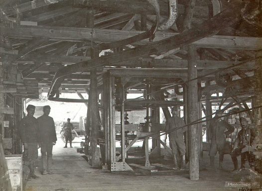 Two people walk through a dimly lit, rustic wooden structure with visible beams.