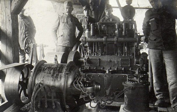 Historic machinery with men in work attire surrounding it, set in a workshop.