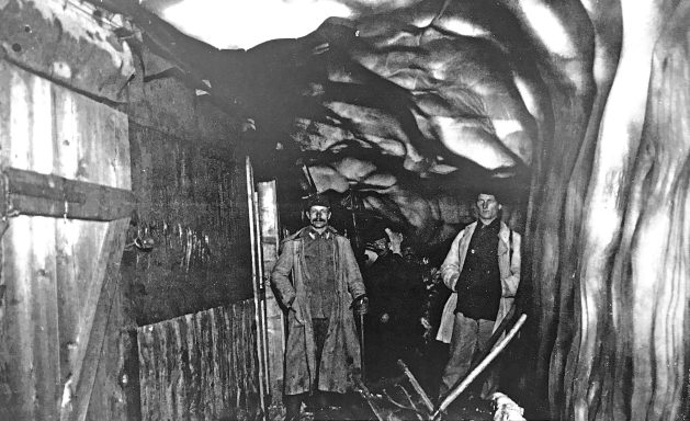 Historic miners standing inside a dimly lit underground tunnel.