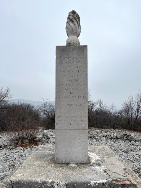 Stone monument with a carved decorative element on top, surrounded by sparse vegetation.
