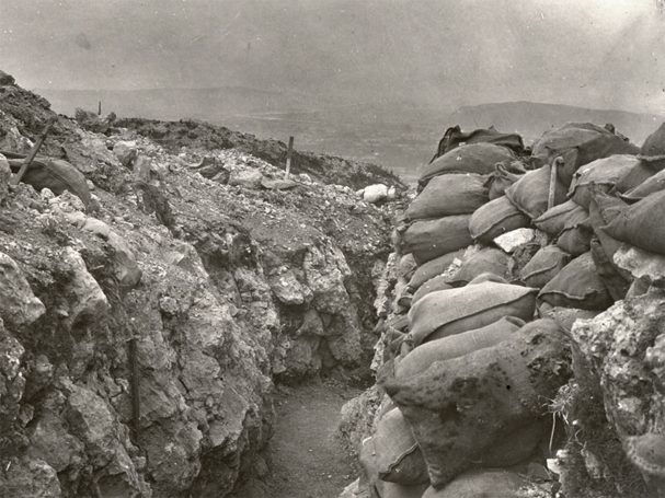 A black and white photograph of a trench surrounded by sandbags.