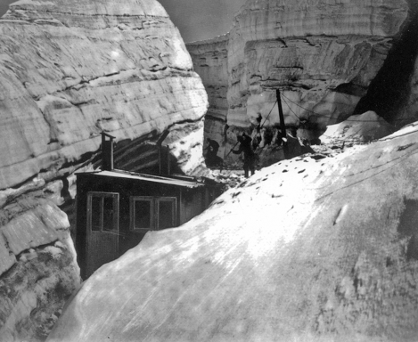 Historic black and white photo of a railway near rocky cliffs, with people visible.