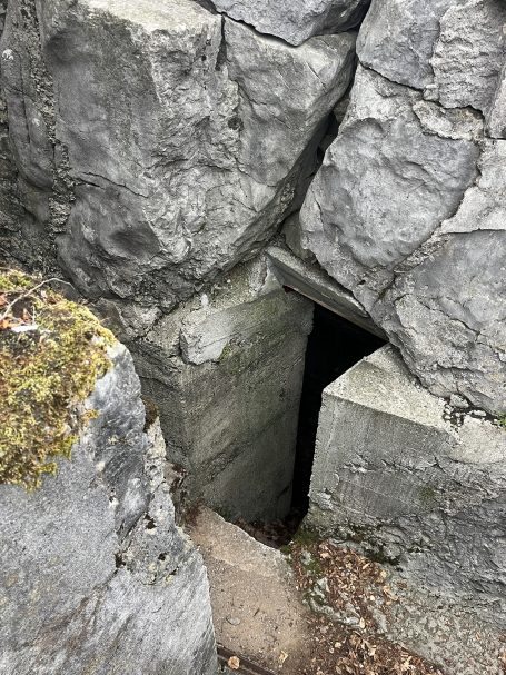 Narrow opening in rocky terrain, leading into a dark cavity.