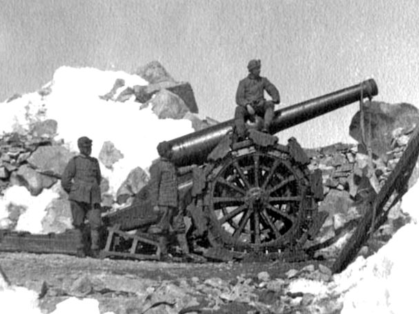 Two soldiers operating a large cannon beside snow-covered rocks.