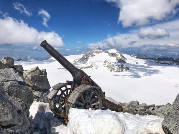 Old cannon on rocky terrain with snow-covered mountains in the background.