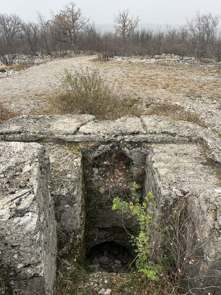 A stone structure with a small opening, surrounded by barren land and sparse vegetation.