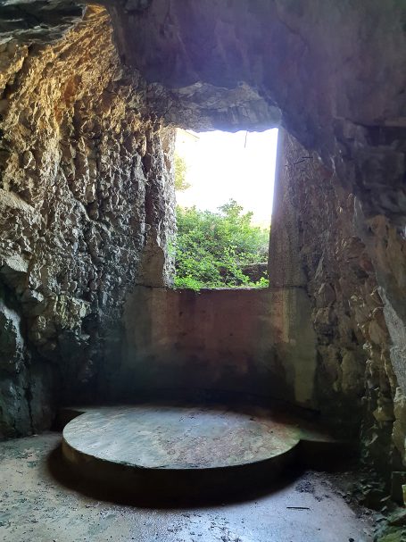 Stone structure with a circular platform and a window opening to greenery outside.