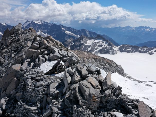 Rocky mountain peak with snow and blue sky, surrounded by distant mountains.