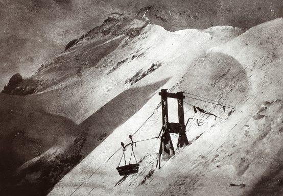 Snow-covered mountain with a cable car station and a suspended basket.