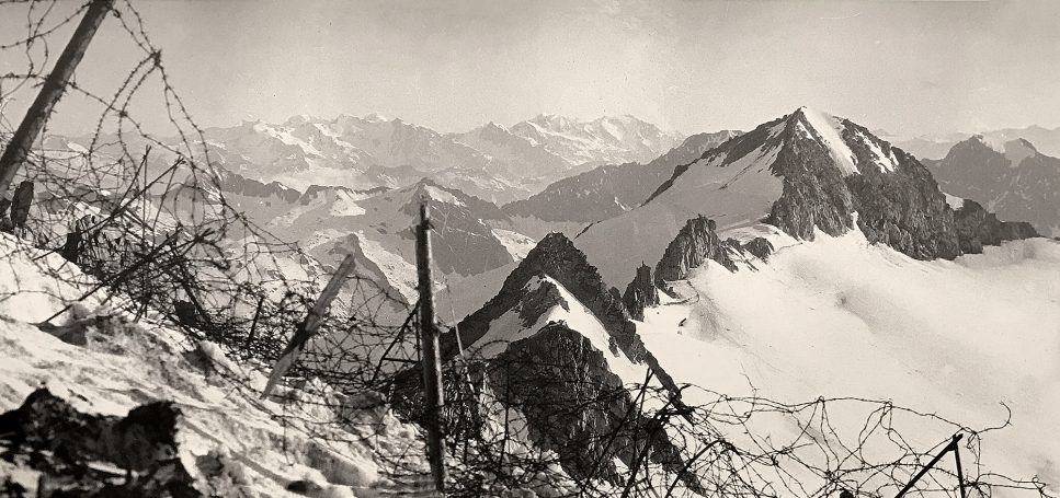 Snowy mountain landscape with peaks and barbed wire in the foreground.