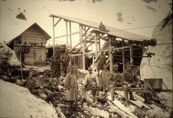 Historical black-and-white photo of miners and a wooden structure in a mountainous area.