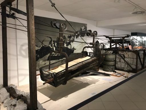 Ski lift equipment displayed in a museum setting with wooden supports and metal machinery.