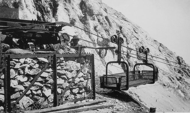 Historic mountain cable car transporting passengers and goods near rocky terrain.