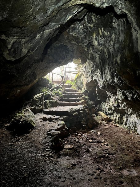 Dark cave entrance with rocky walls, leading to a light-filled pathway.