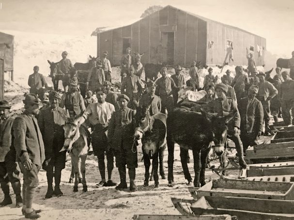 A group of historical workers with horses and buildings in a rural setting.