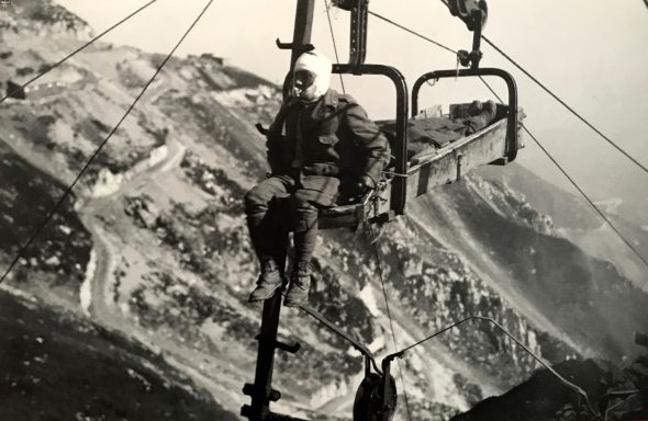 A man riding a ski lift with mountains in the background.